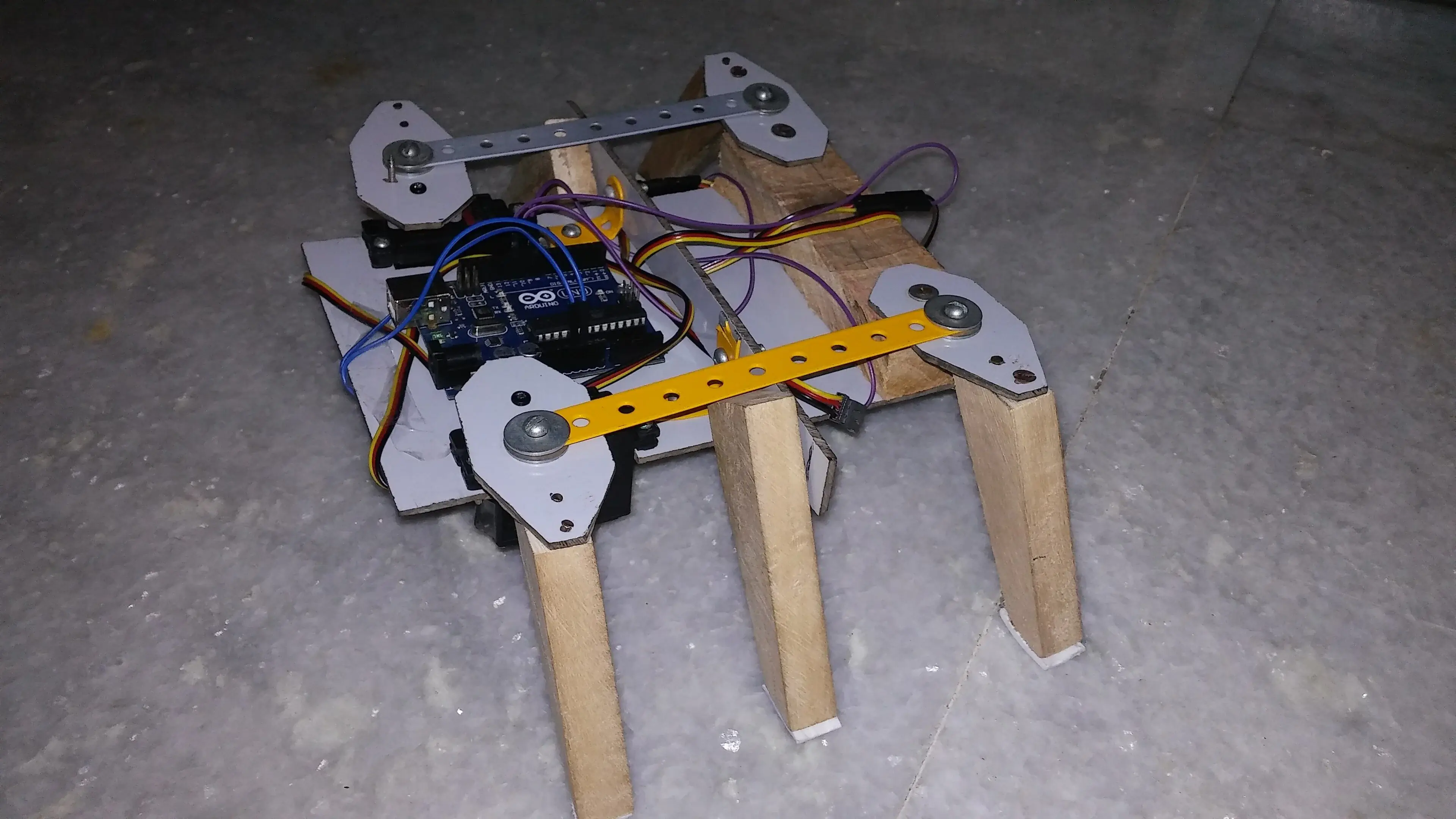 A six-legged experimental robot with wooden legs, metal linkages and an exposed Arduino controller.