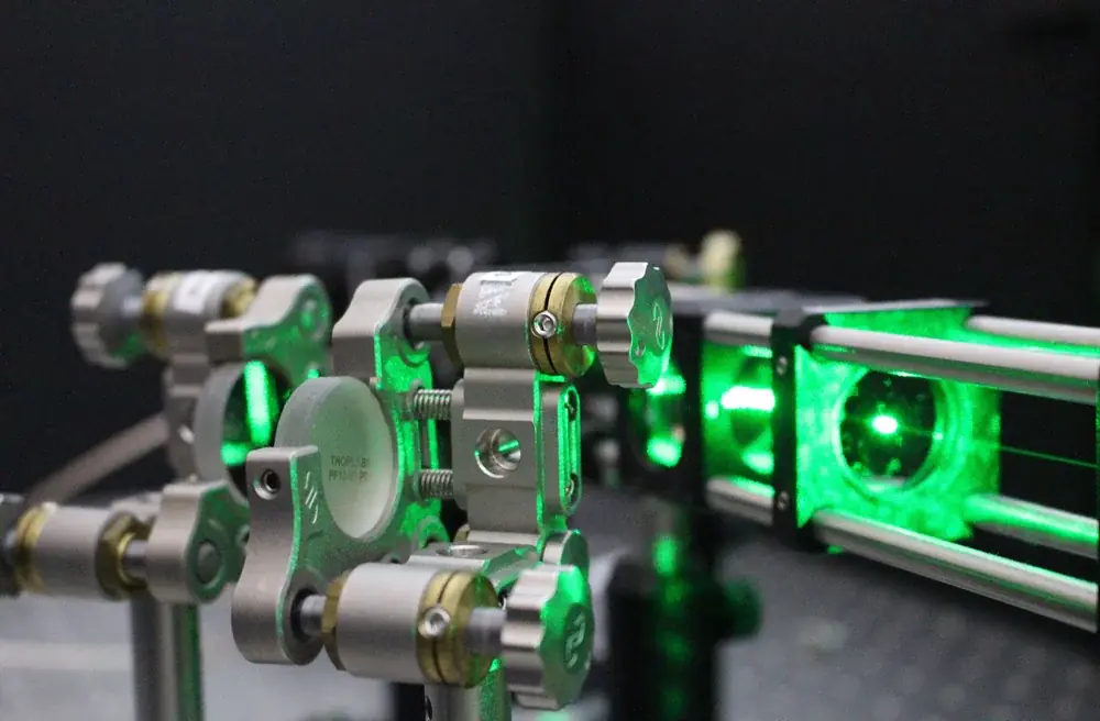 Green laser light passes through lenses and adjustable mounts on an optical table.