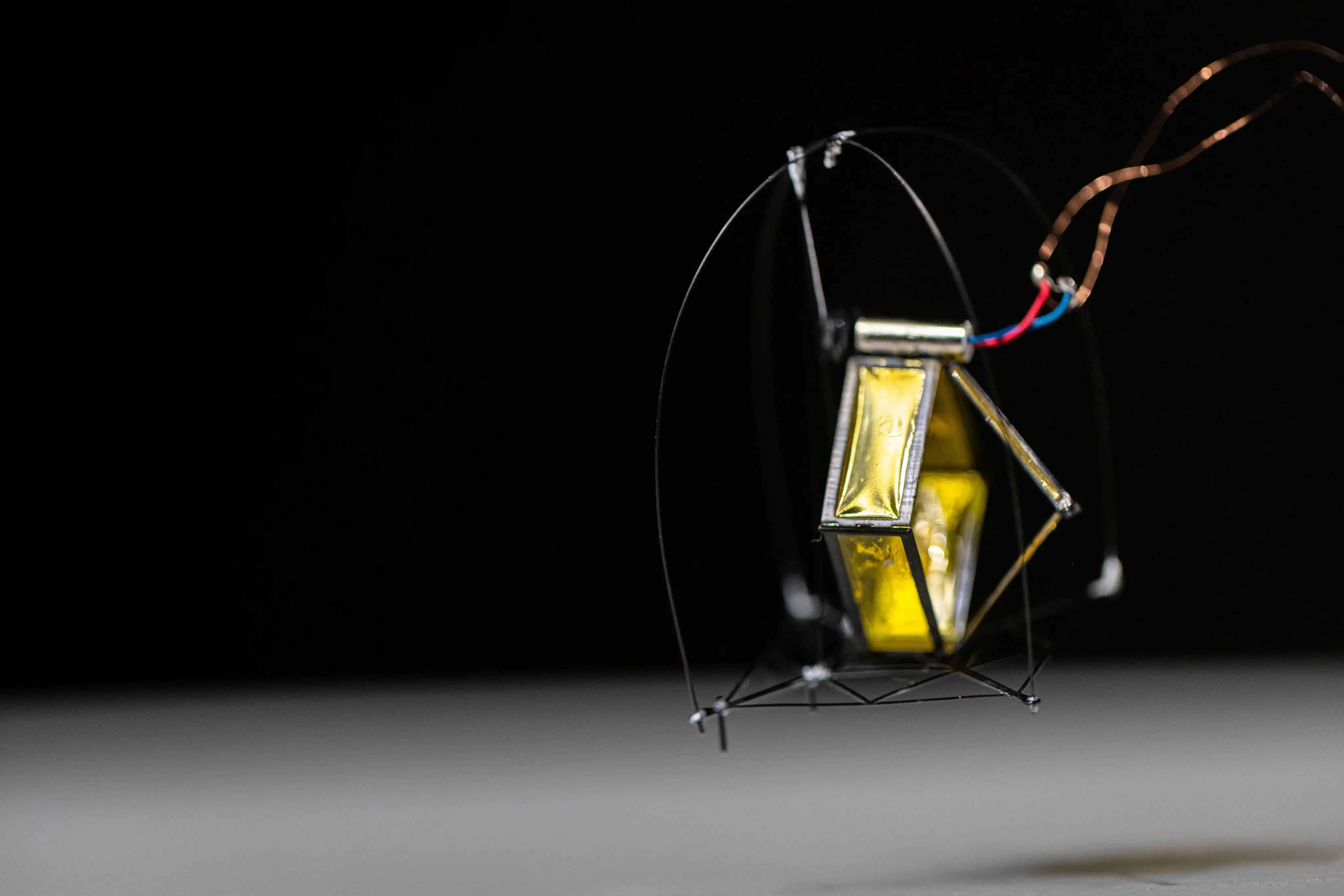 UW’s small black-and-gold DirectHop prototype leaps from a tabletop, with its roll cage and power wires visible.
