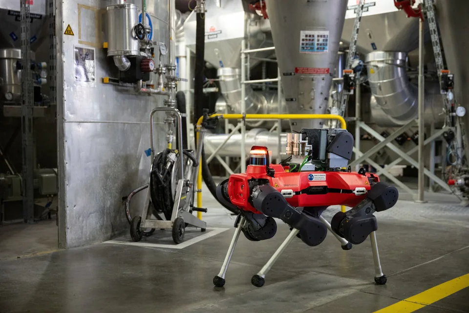 Red ANYmal X quadruped inspection robot walking through an industrial plant with process equipment.