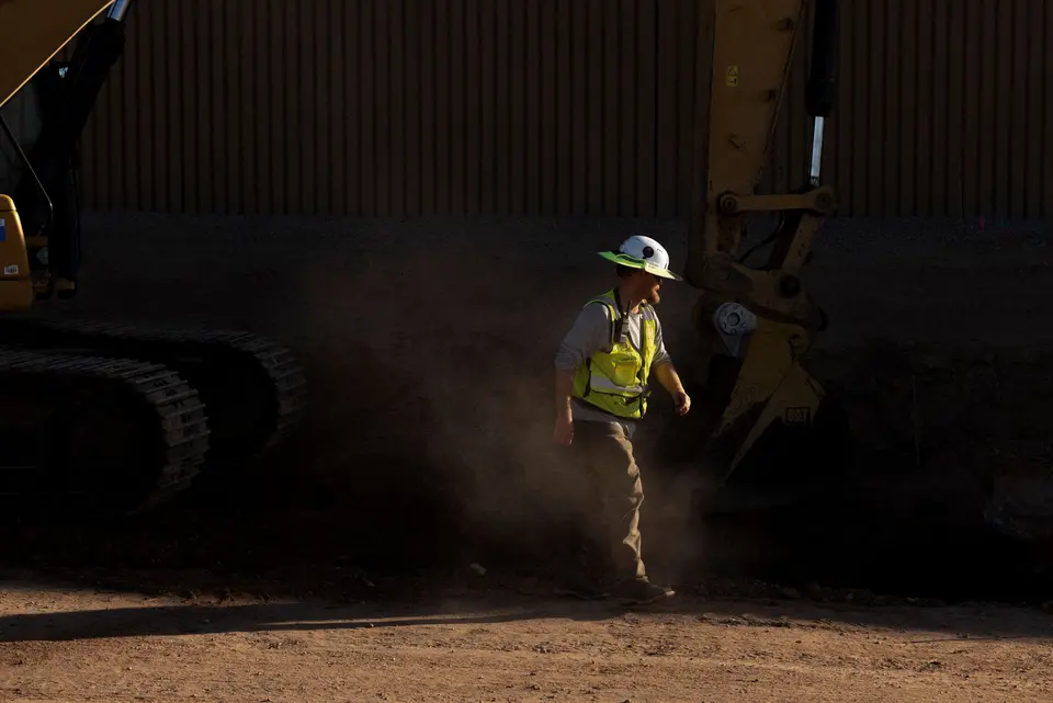 A construction worker standing beside a large excavator at an active earthmoving site.