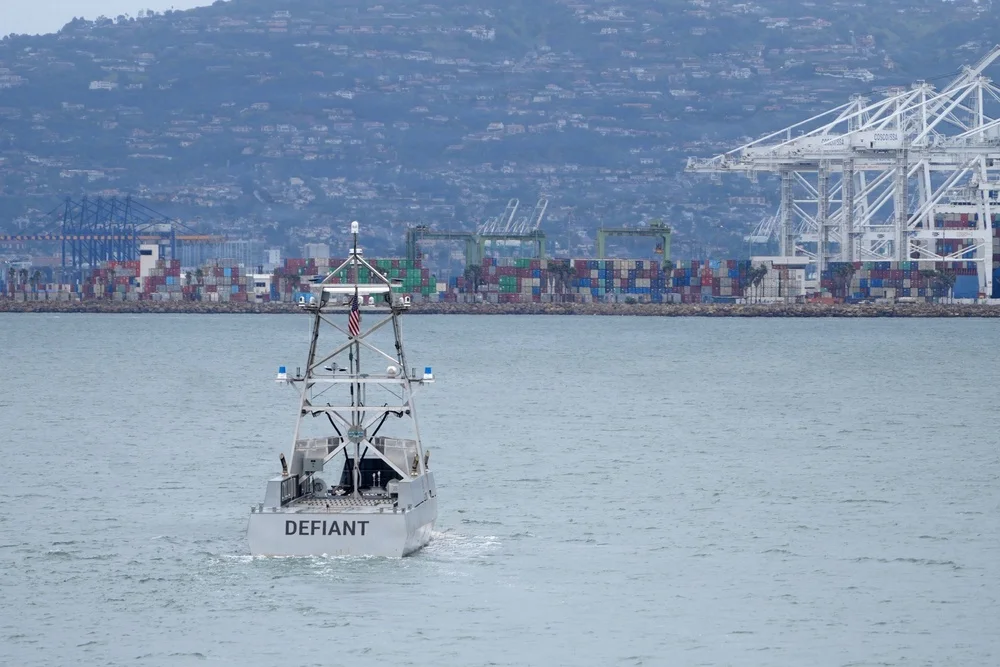 USX-1 Defiant unmanned surface vessel underway near a container port.