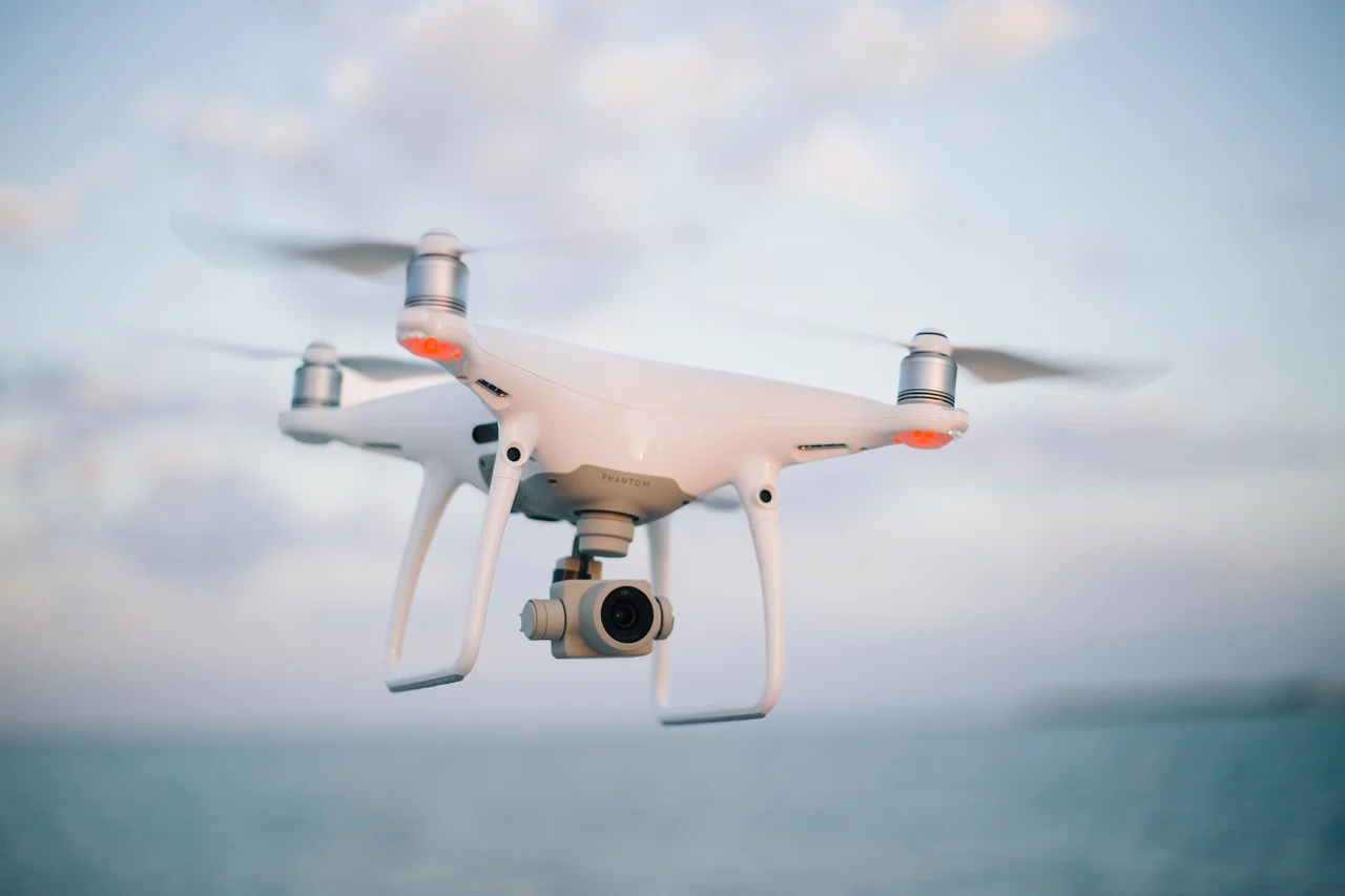 White quadcopter camera drone flying against a blue sky.