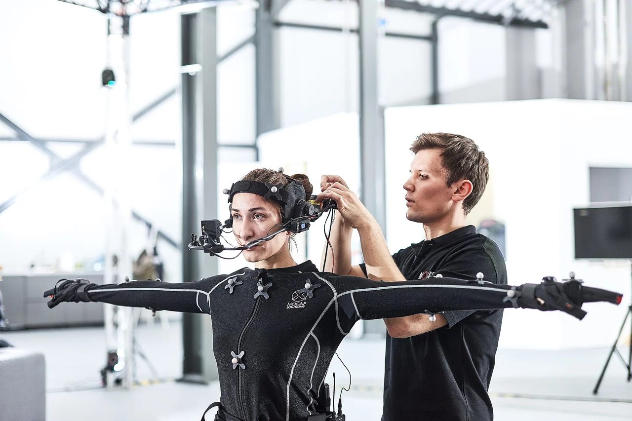 Performer wearing a motion capture suit while a technician adjusts the head-mounted camera.